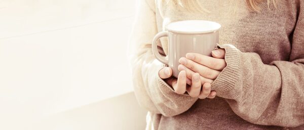 Hands holding a warm mug near a window in the morning